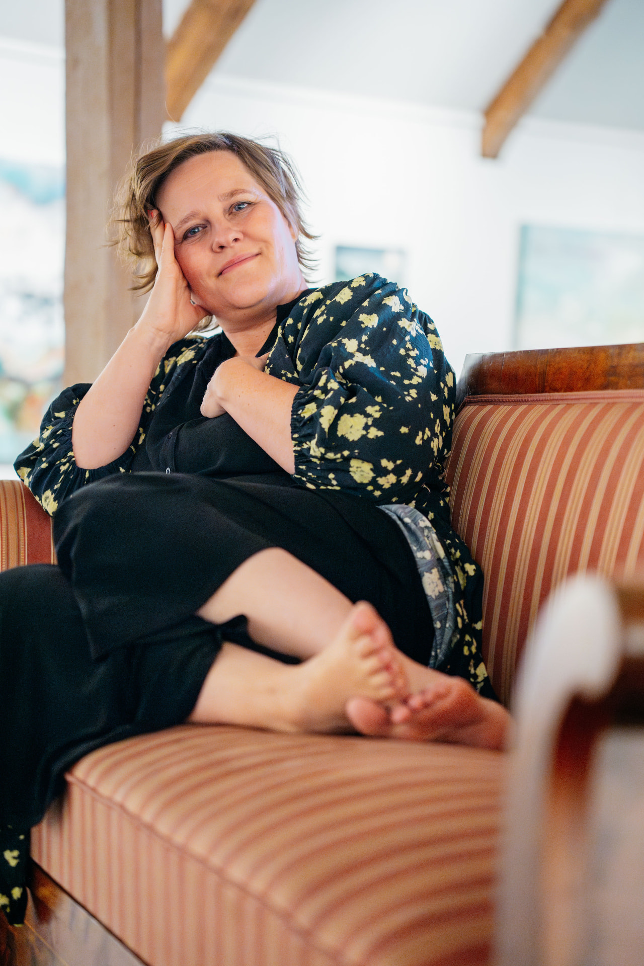 Carmen relaxing on a striped sofa, looking towards the camera with a soft smile