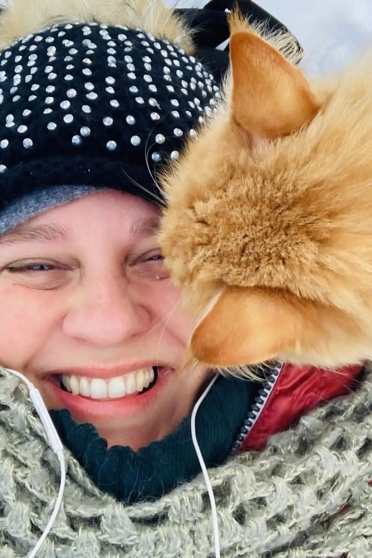 Carmen smiling with her eyes closed beside her fluffy golden cat in the snow